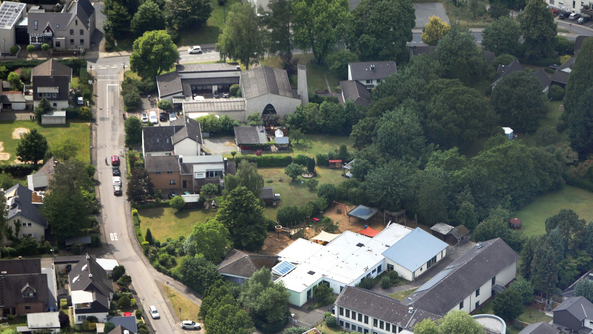Auf einem Luftbild sind eine Kirche, Häuser, Gärten und Bäume zu sehen.