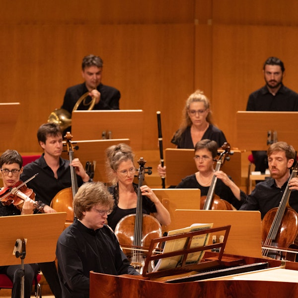 Der Pianist sitzt an einem Hammerklavier, hinter ihm eine Reihe Cellisten.