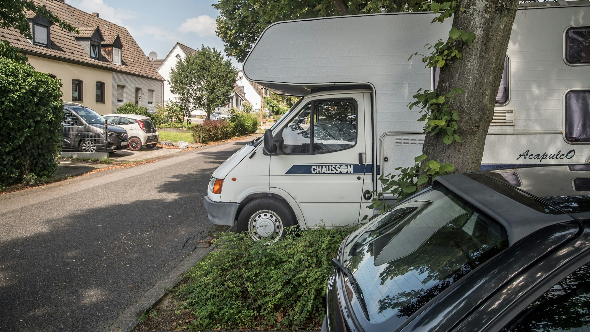 Ein Wohnmobil im öffentlichen Raum auf einem schattigen Parkplatz in Schlebusch.