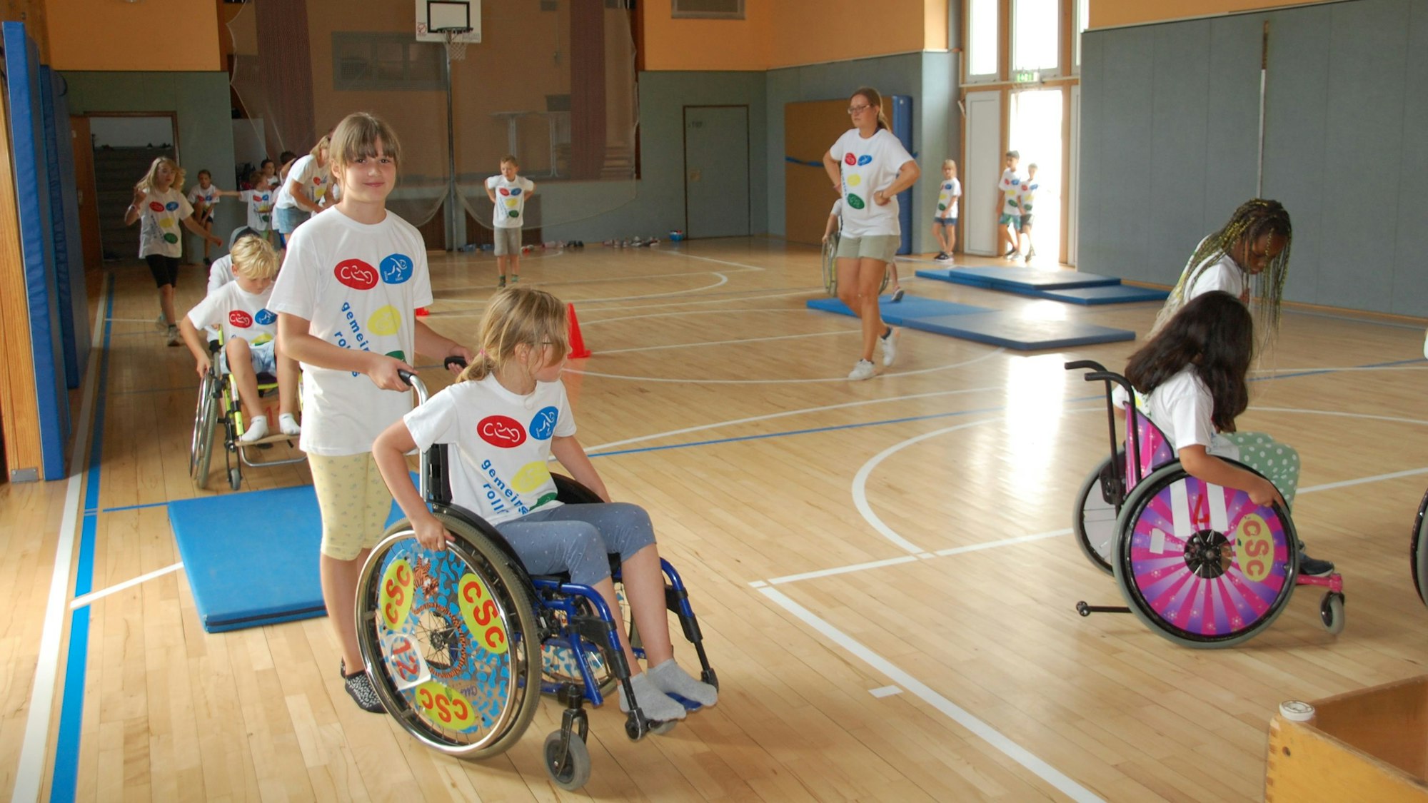 Kinder testen Rollstühle in der Turnhalle.