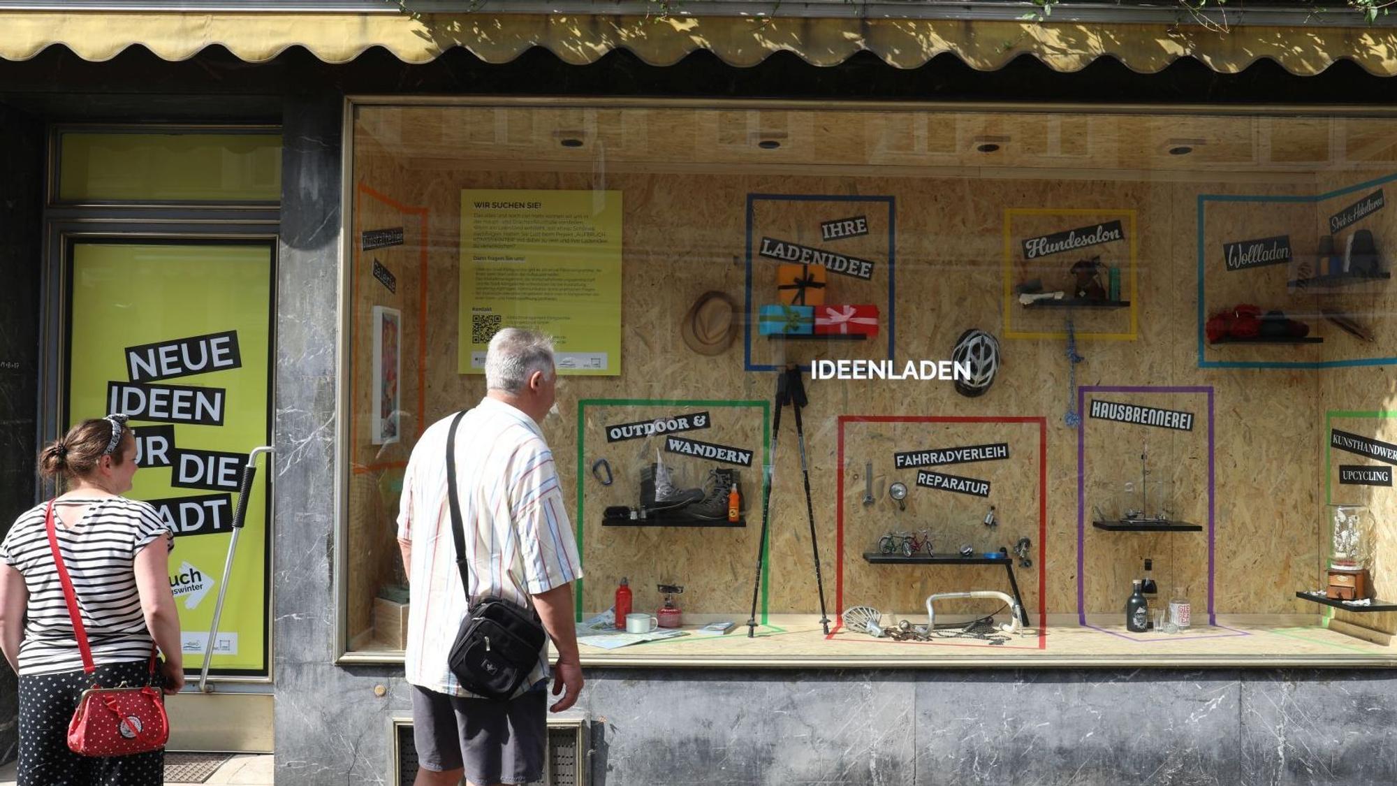 Eine Frau und ein Mann stehen vor einem Schaufenster mit dem Schriftzug „Ideenladen“