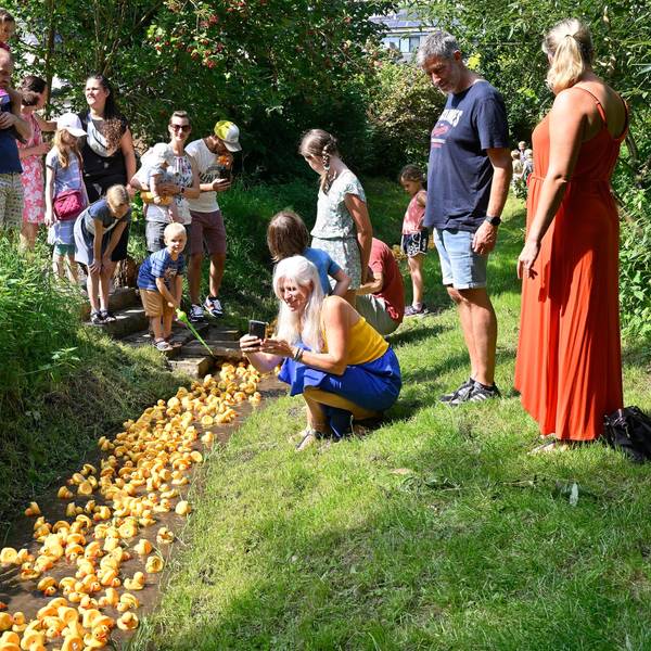 Menschen stehen am Bach und beobachten das Entenrennen in Overath-Immekeppel