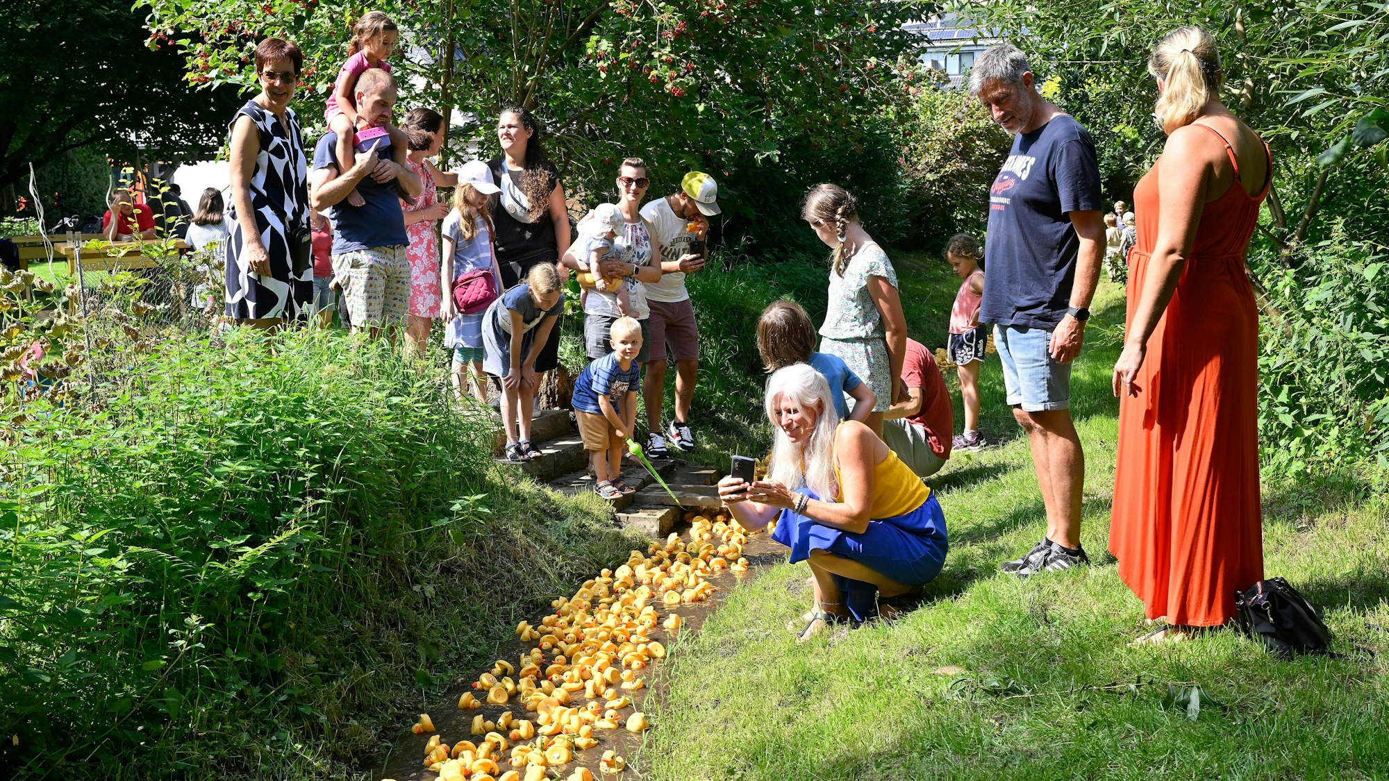 Menschen stehen am Bach und beobachten das Entenrennen in Overath-Immekeppel