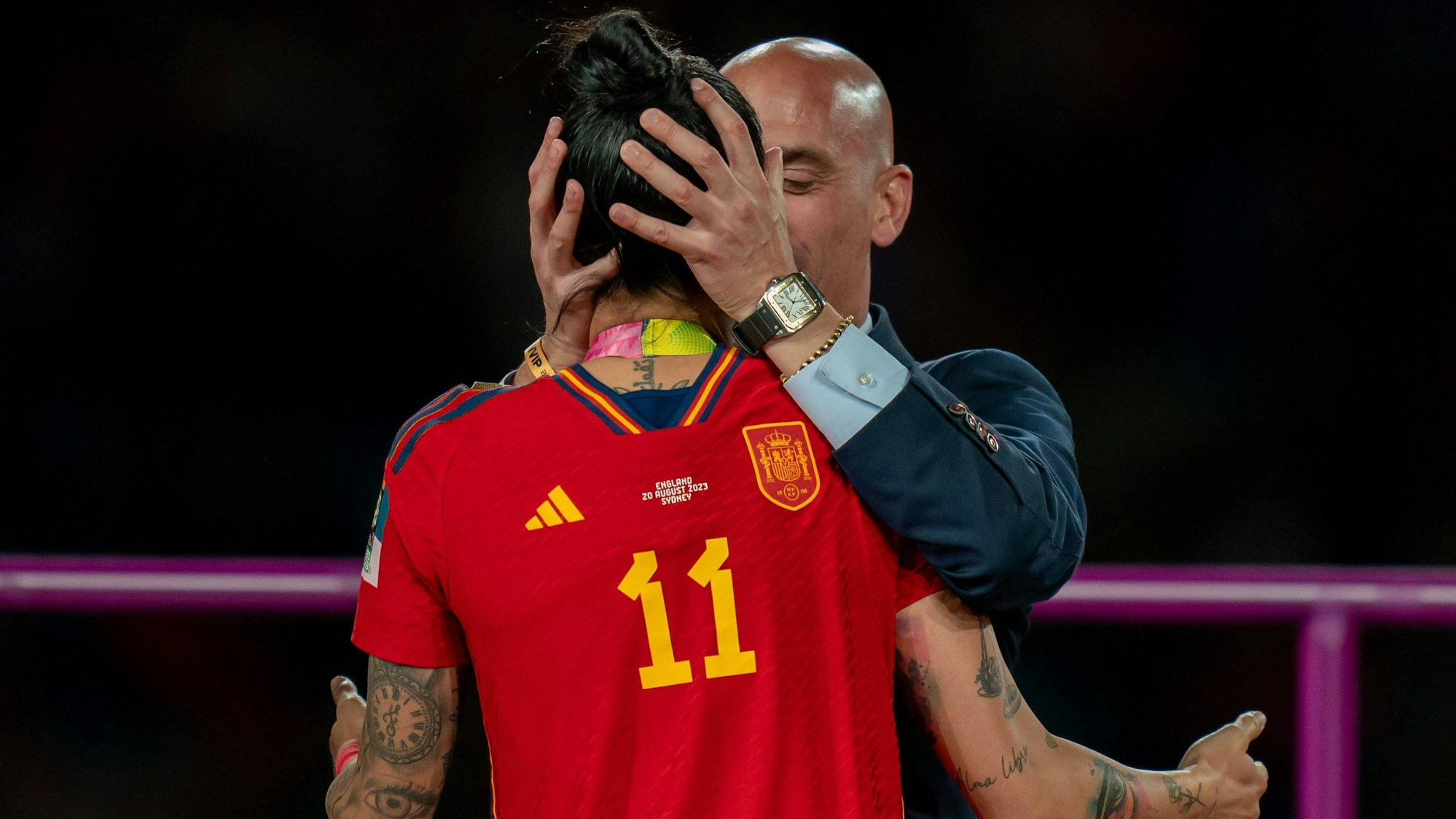 Luis Rubiales, Chef des spanischen Fußballverbands, ergreift mit beiden Händen den Kopf von Nationalspielerin Jennifer Hermoso, um sie zu küssen. Die Spielerin ist von hinten zu sehen, ihre Arme hält sie vom Körper abgewinkelt, ohne Rubiales zu berühren.