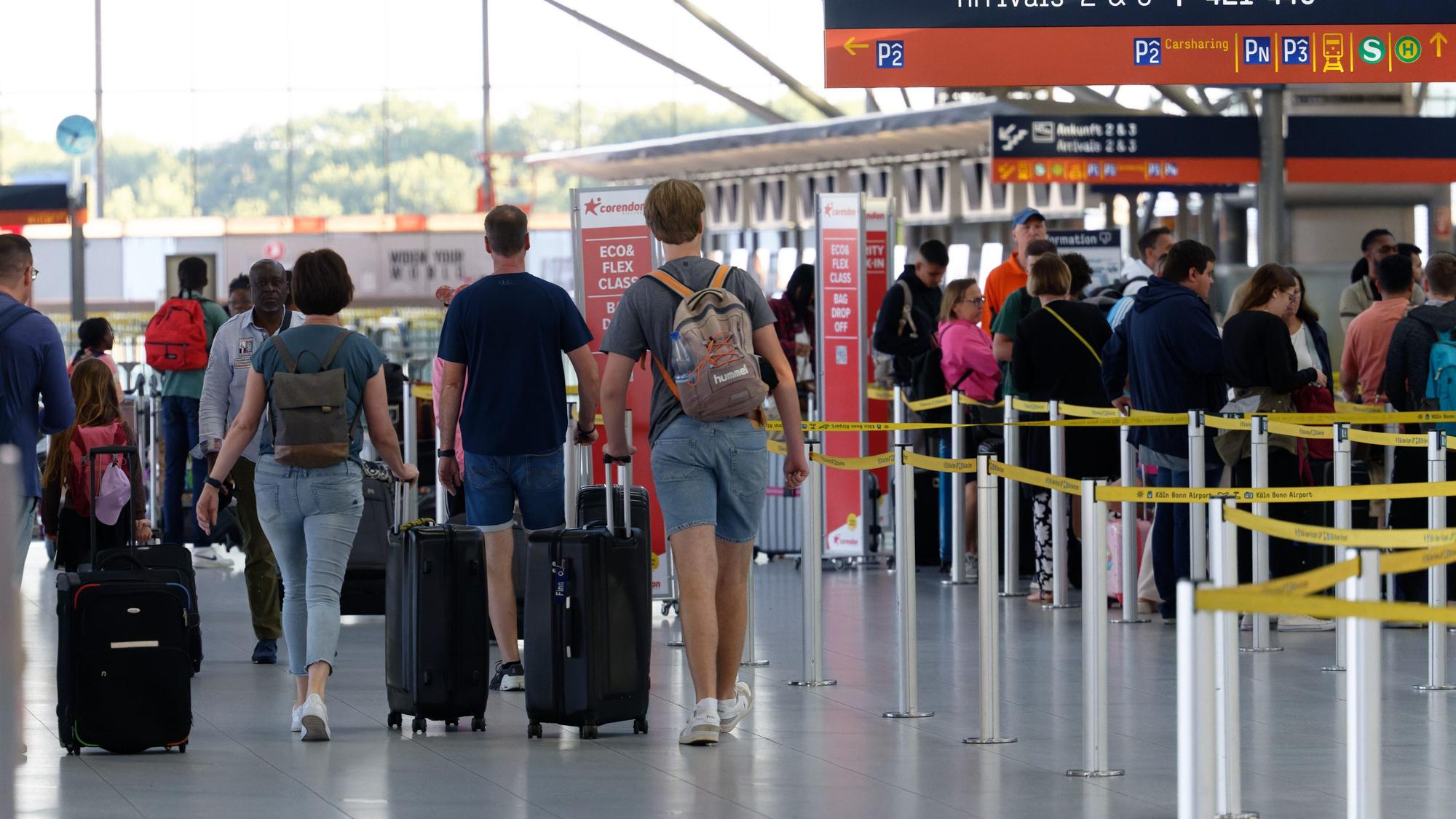 Reisende gehen im Flughafen Köln/Bonn durch die Abflughalle.