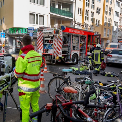 Rettungskräfte der Berufsfeuerwehr stehen bei einem Wohnungsbrand in der Huhnsgasse neben einer fahrbaren Trage.