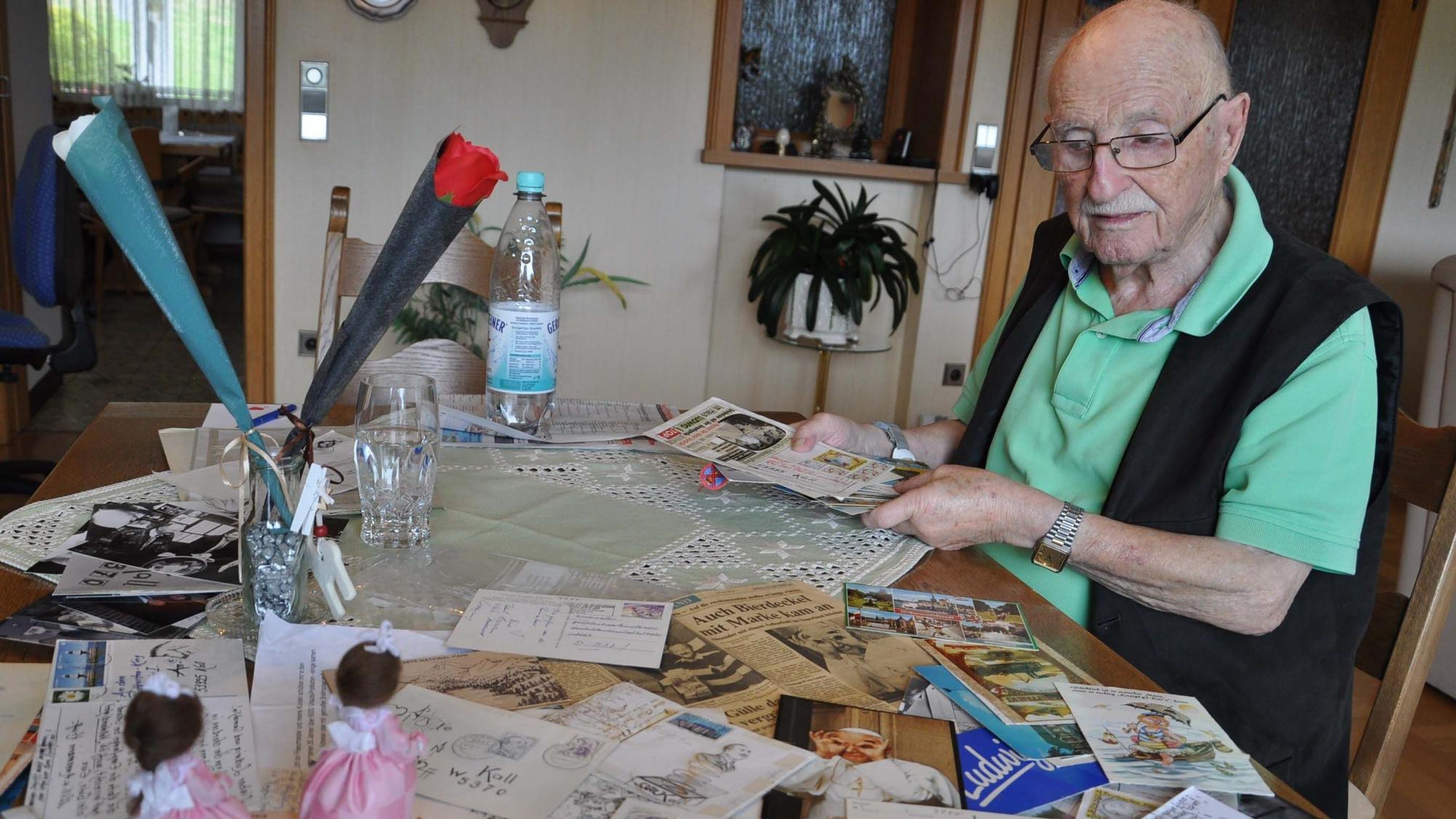 Ludwig Theisen sitzt an einem Tisch. Vor dem 89 Jahre alten Mann sind einige der 6000 Postkarten ausgebreitet, die er in den vergangenen Jahrzehnten erhalten hat.