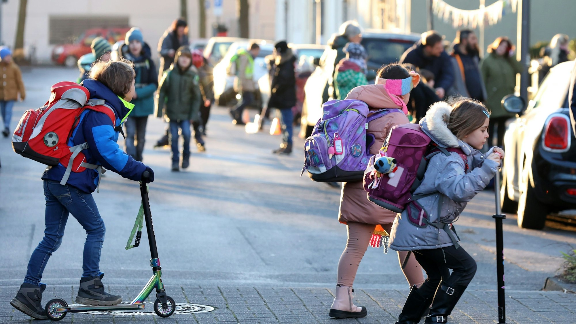 Kinder mit Roller und zu Fuß auf dem Weg zur Schule.