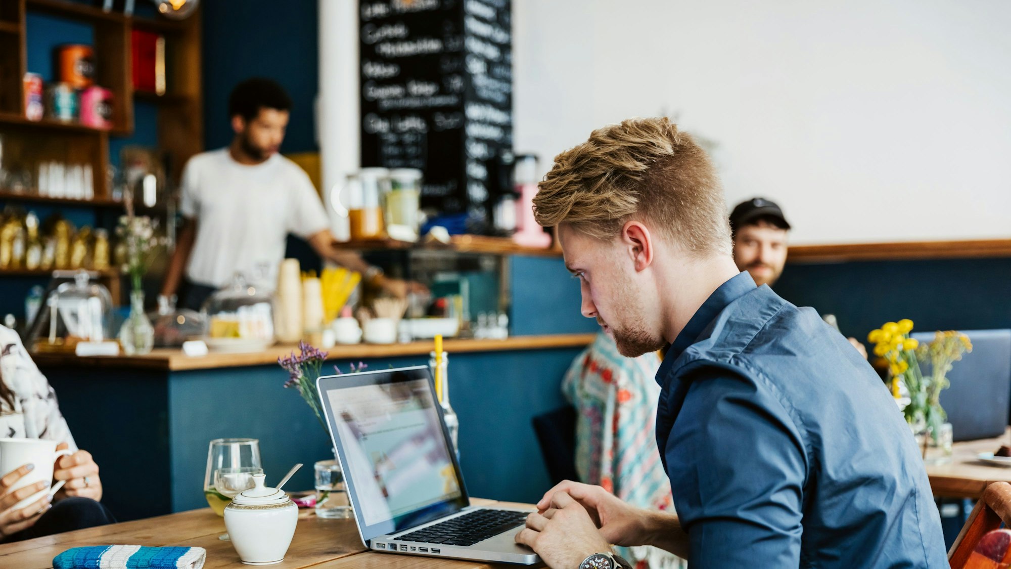 Ein junger Mann arbeitet in einem Café an seinem Laptop.
