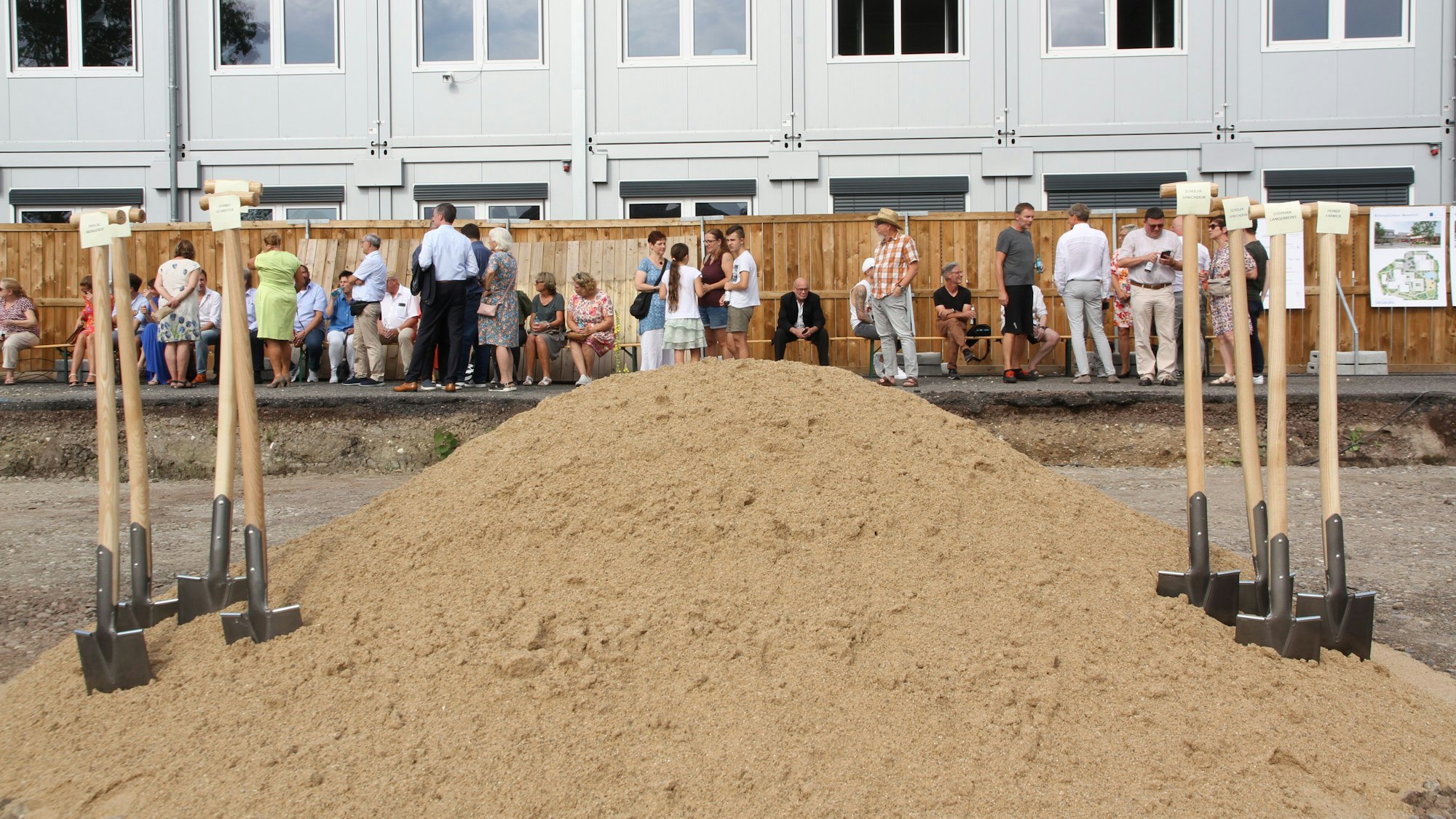 Acht Spaten in einem Sandhaufen, dahinter Raumcontainer