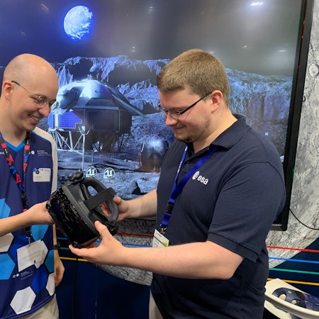 Student David Reiter steht vor einer Simulation der Mondoberfläche. Er unterhält sich mit Florian Salzig, der bei der Hochschule Bonn-Rhein-Sieg studiert und nach seinem Masterabschluss zum DLR gegangen ist.