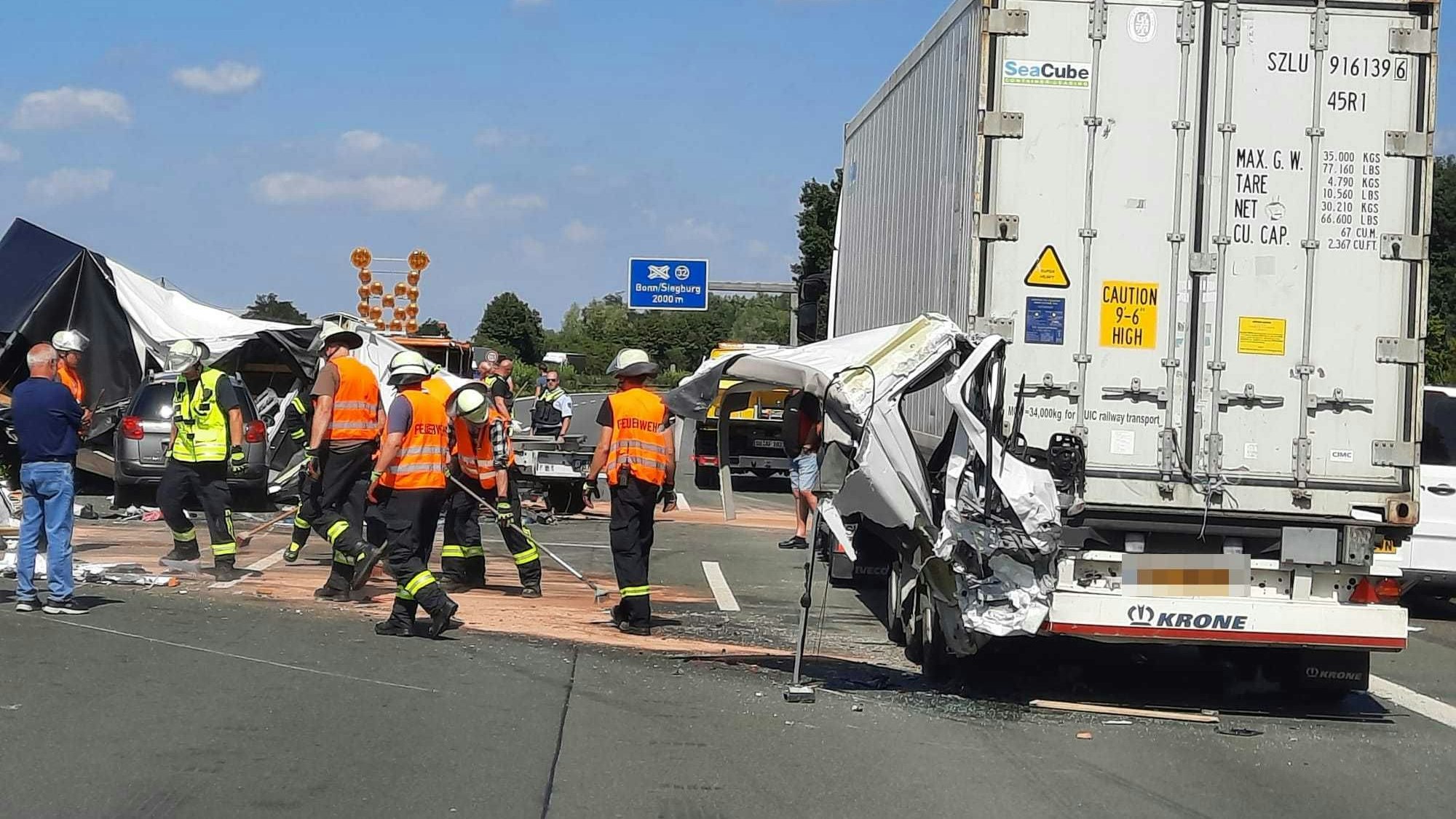 Einsatzkräfte der Feuerwehr streuen auf der Autobahn Betriebsstoffe ab. Im Auflieger des Sattelschleppers stecken Teile der Fahrerkabine eines Transporters.