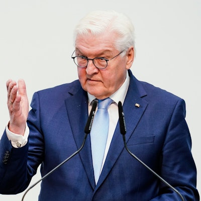 Bundespräsident Frank-Walter Steinmeier steht vor Mikrofonen und hebt eine Hand vor einem weißen Hintergrund.