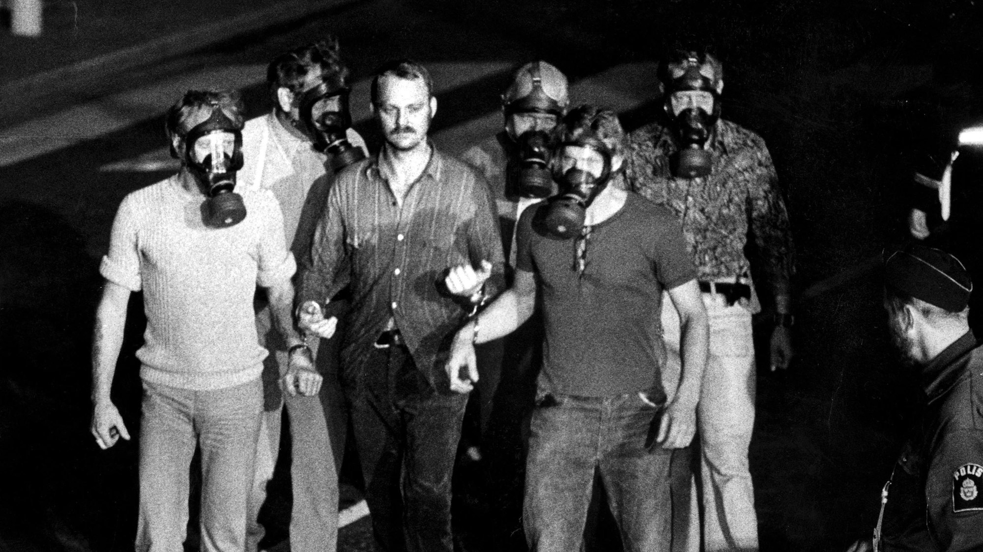 Die Schwarz-Weiß-Aufnahme zeigt fünf Polizisten, die Gasmasken tragen und Jan-Erik Olsson in Handschellen abführen. (Archivbild)