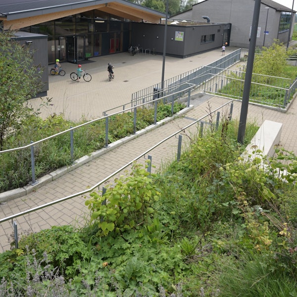 Ein modernes Schulgebäude,davor fahren drei Kinder Fahrrad.