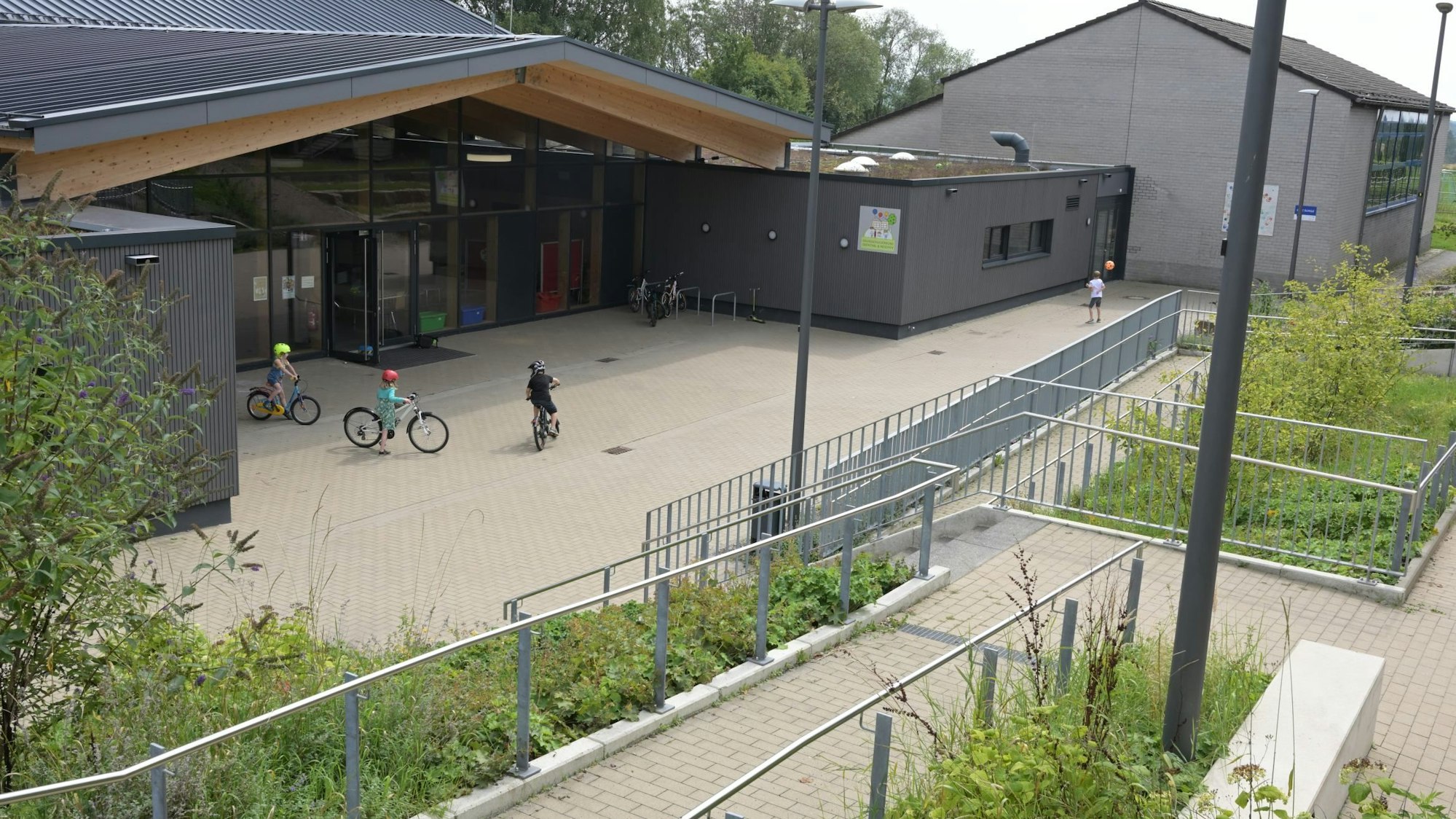 Ein modernes Schulgebäude,davor fahren drei Kinder Fahrrad.