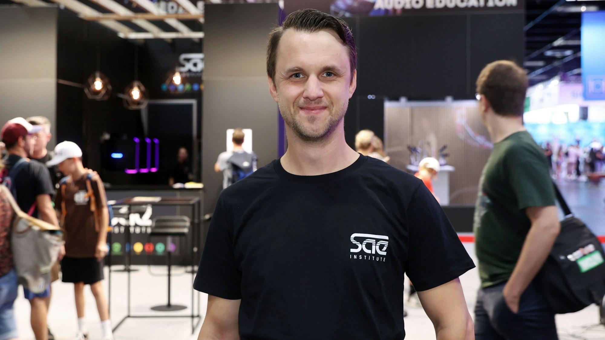 Lukas Middelmann steht auf der Gamescom und lächelt in die Kamera.