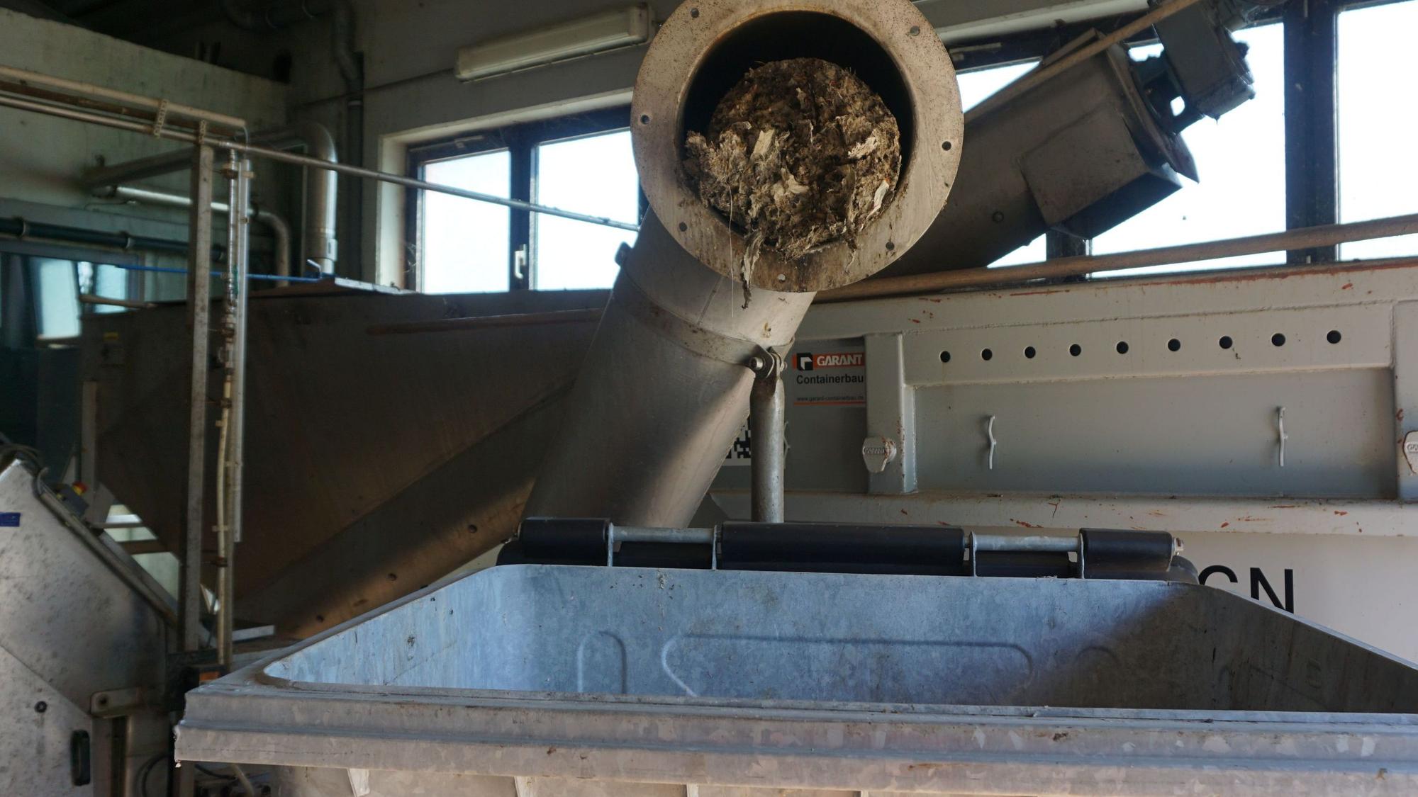 Das Bild zeigt ein geöffnetes Rohr. Abfall presst sich heraus. Darunter steht ein Container.