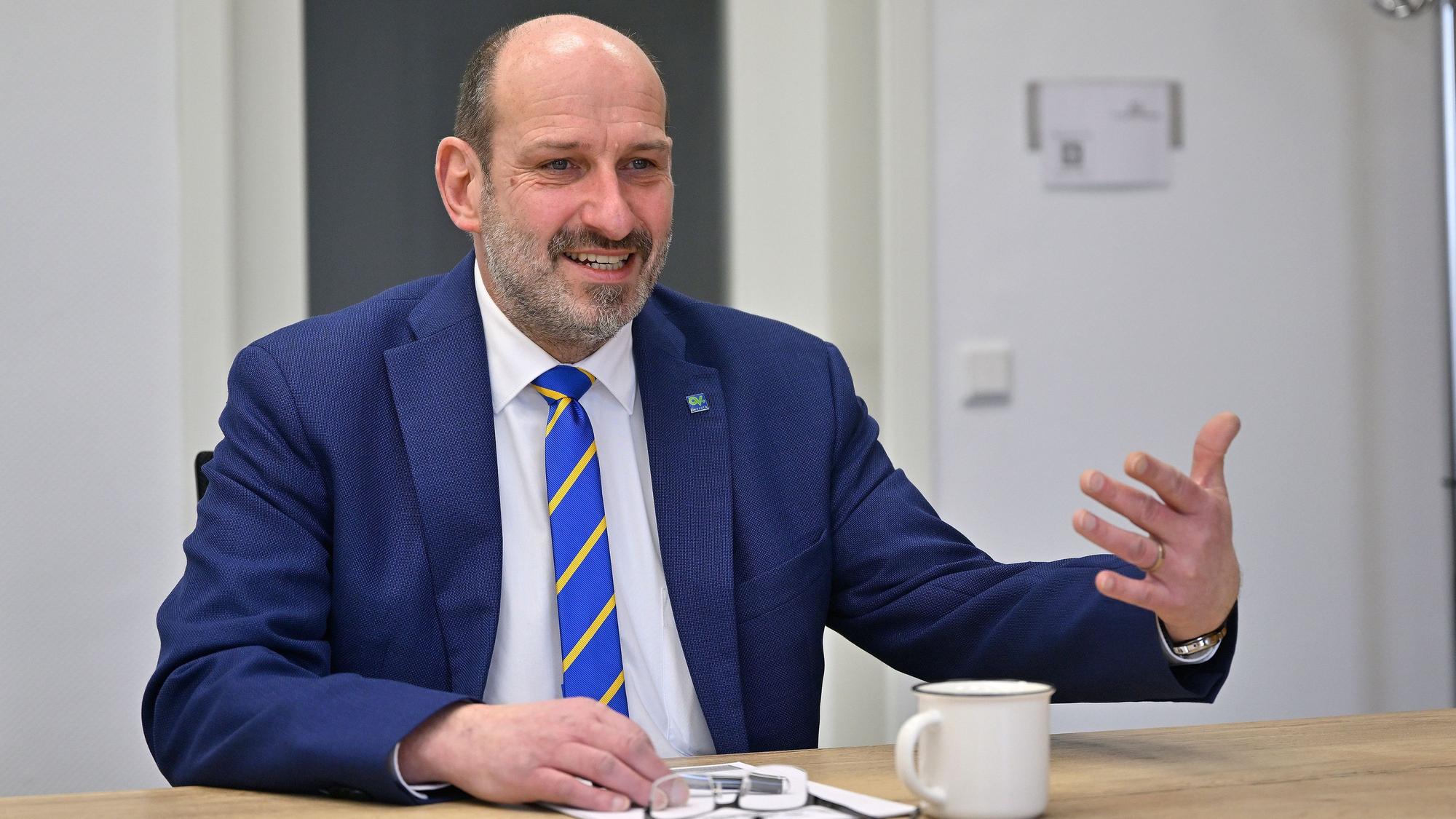 Overaths Bürgermeister Christoph Nicodemus sitzt an einem Tisch und spricht.