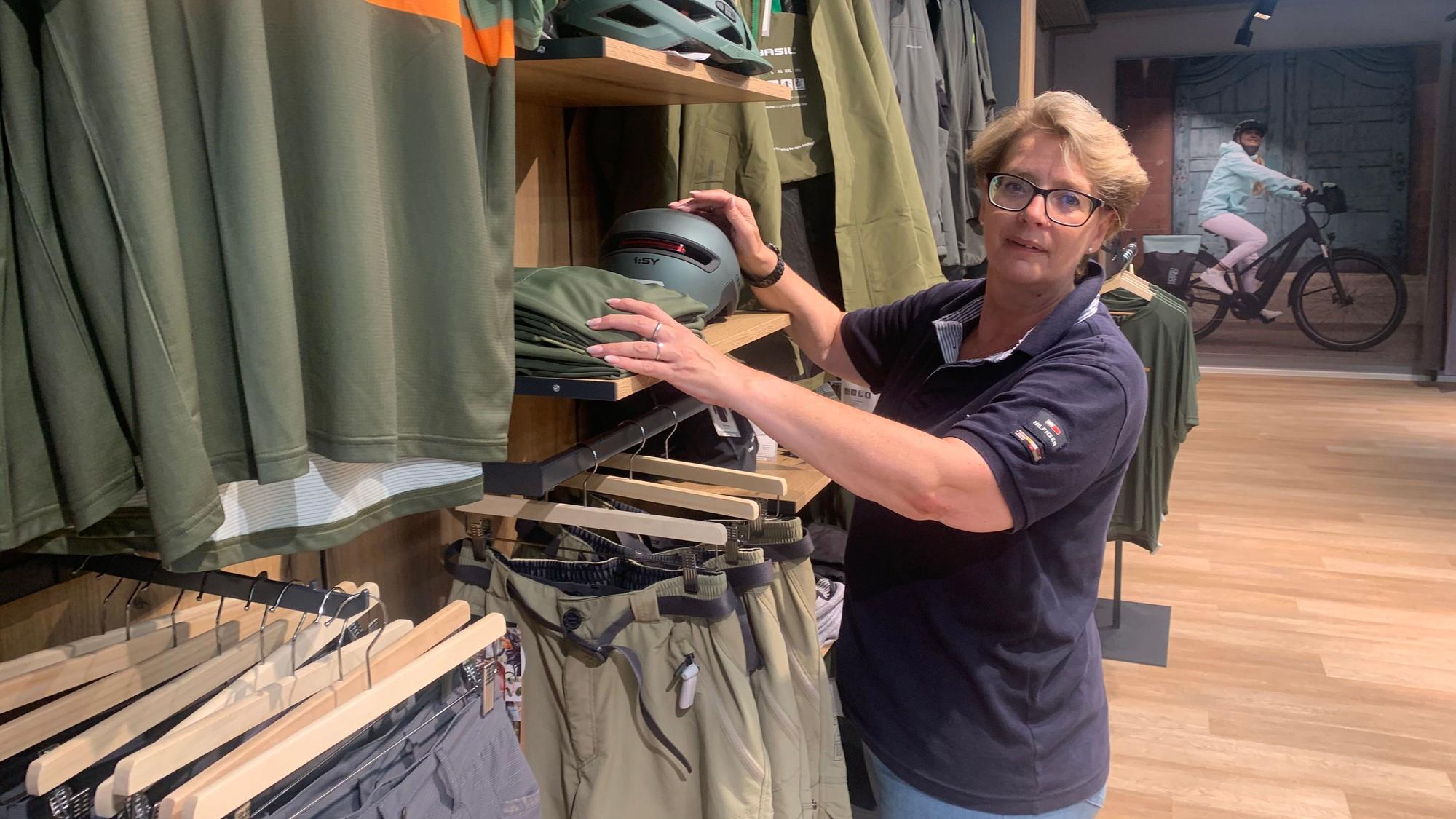 Textil-Abteilungsleiterin Sylke Burmeister rückt Hemden zurecht, die auf Bügeln an einer Stange hängen.