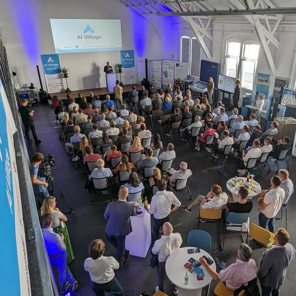 Volle Sitzreihen und Stellwände in einem Saal.