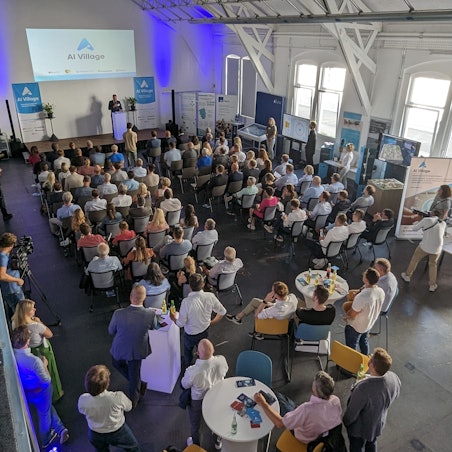 Volle Sitzreihen und Stellwände in einem Saal.