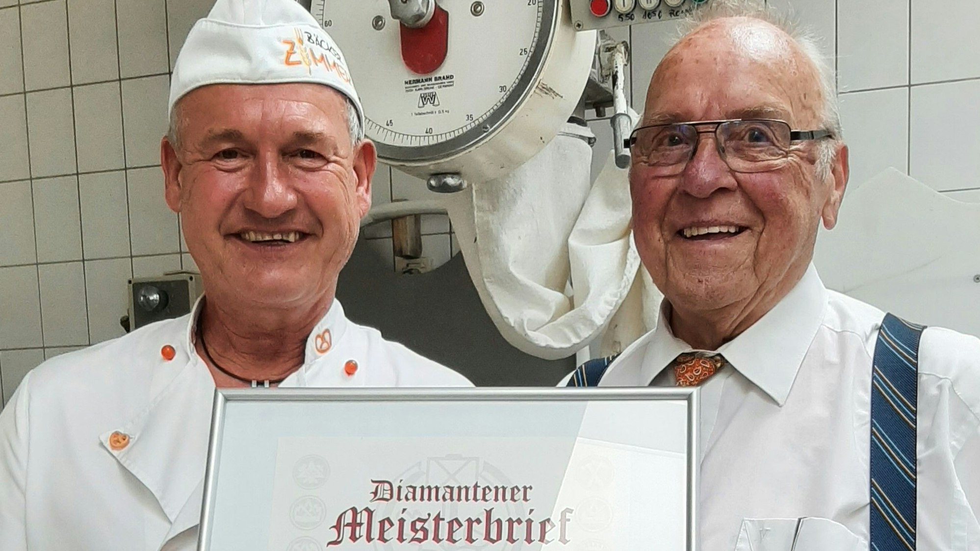 Zwei Männer stehen in einer Backstube: Obermeister Siegwin Zimmer (l.) überreicht Herbert Poth den diamantenen Meisterbrief.