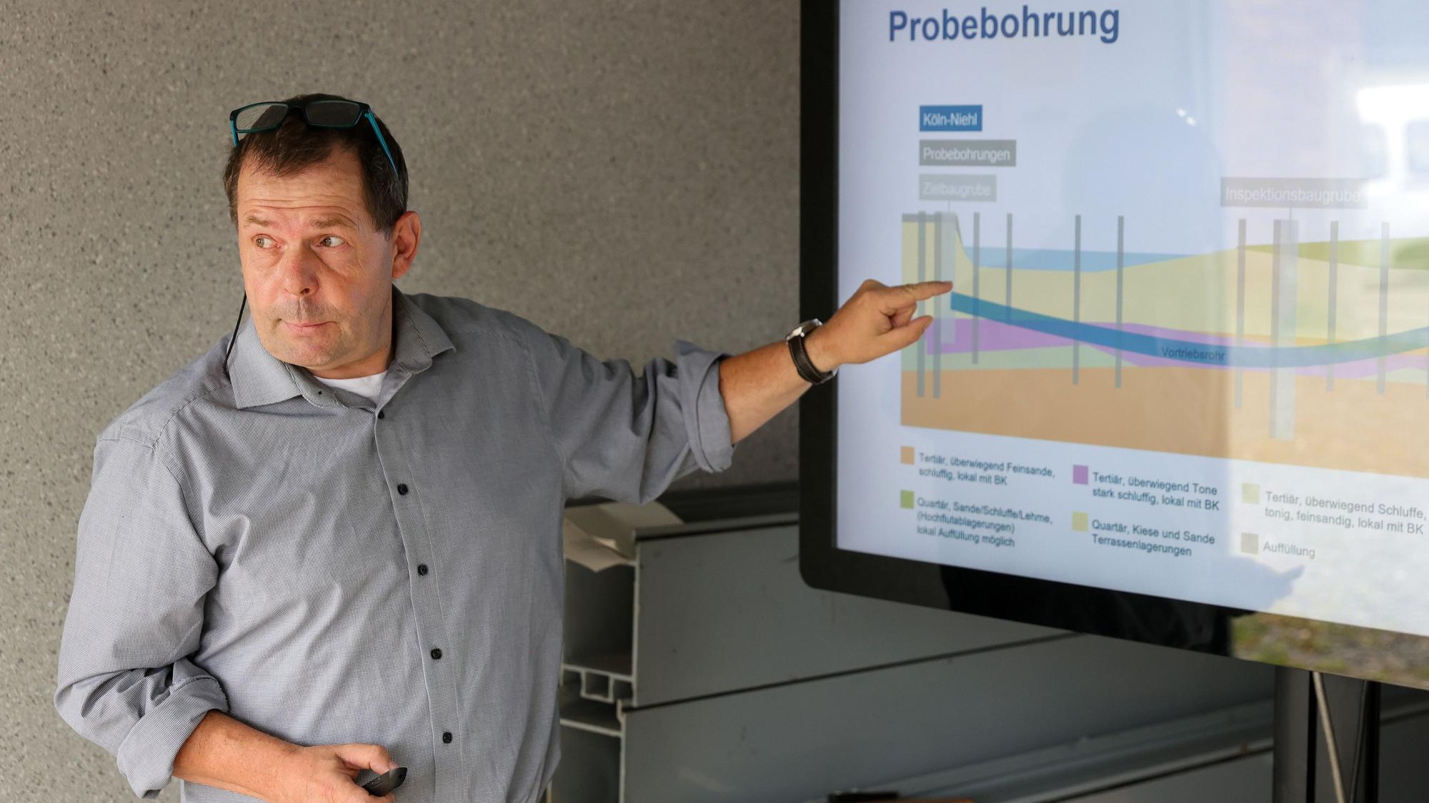 Mann mittleren Alters in einem grauen Hemd, der auf eine Grafik auf einem Bildschirm zeigt