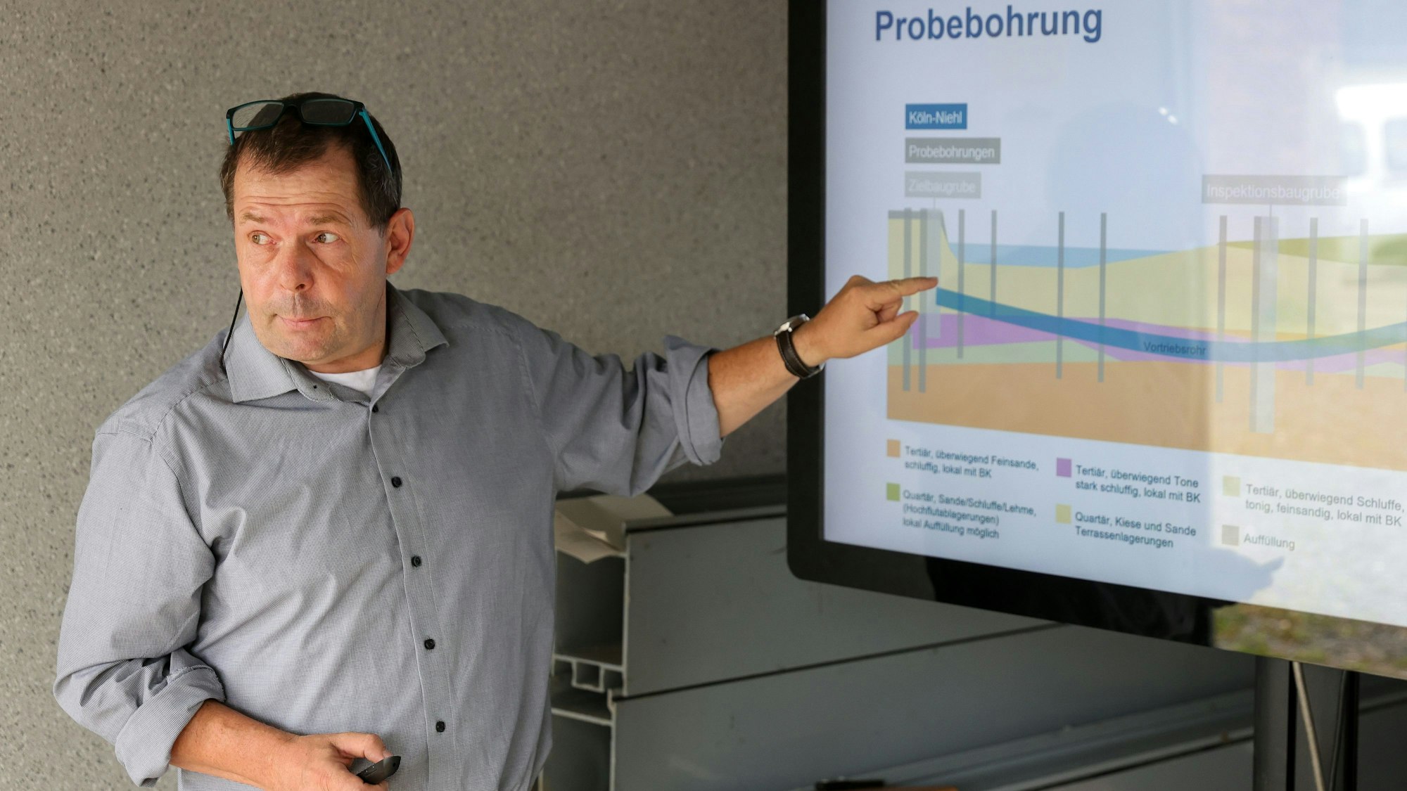 Mann mittleren Alters in einem grauen Hemd, der auf eine Grafik auf einem Bildschirm zeigt