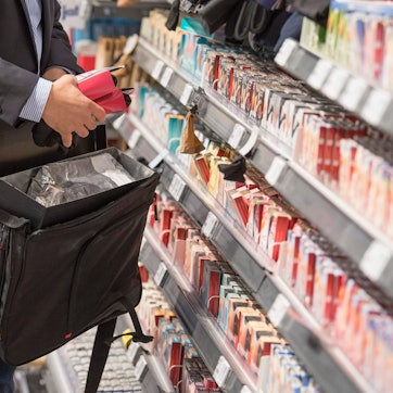 Das Bild ist ein Symbolfoto und zeigt, wie ein Mann Gegenstände aus einem Regal in seine Tasche steckt.