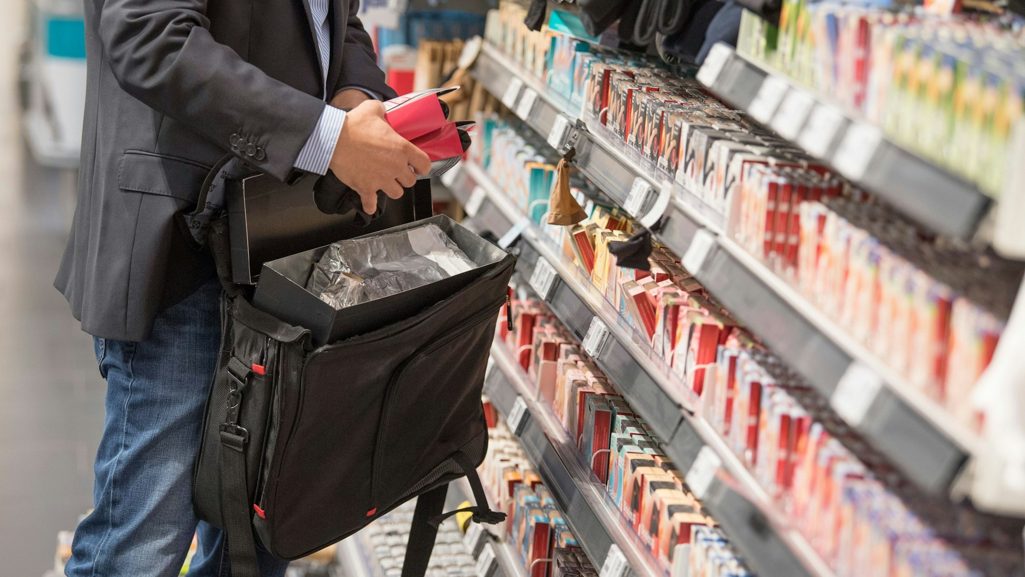 Ein Mann packt Waren aus einem Regal in eine mitgeführte Tasche.