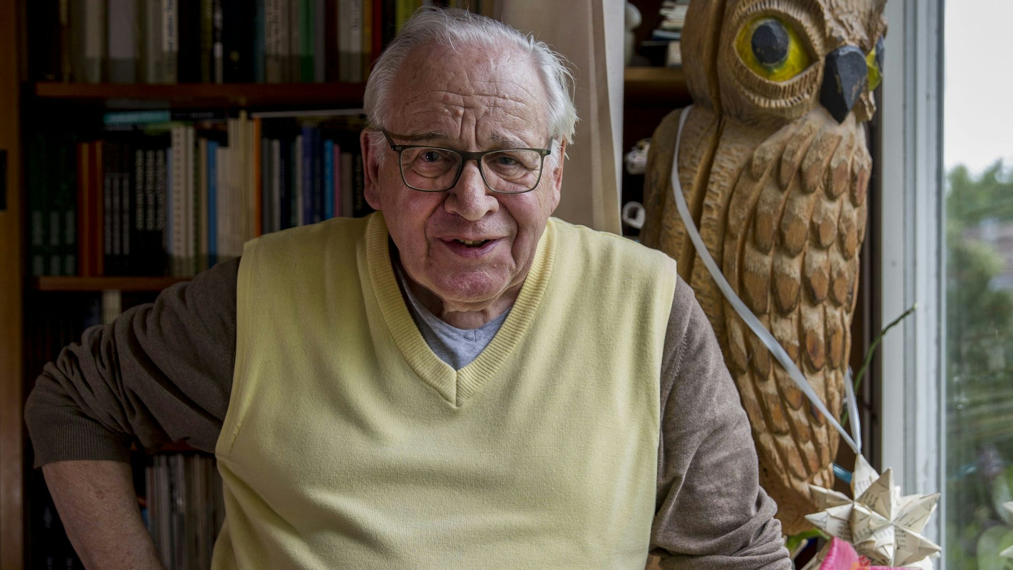 Porträt eines alten Mannes mit grauen Haaren, Brille und gelbem Pullover in seiner Wohnung