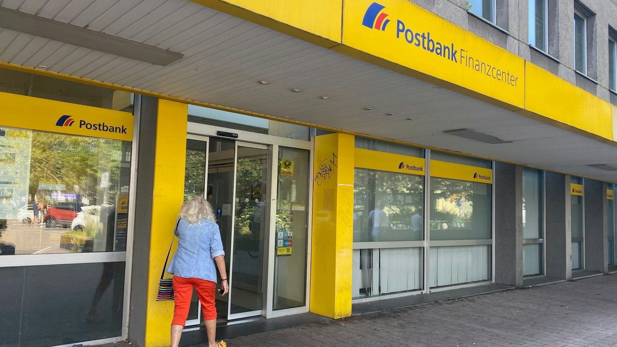 Eine Frau, die von hinten zu sehen ist, geht in die Filiale einer Postbank.