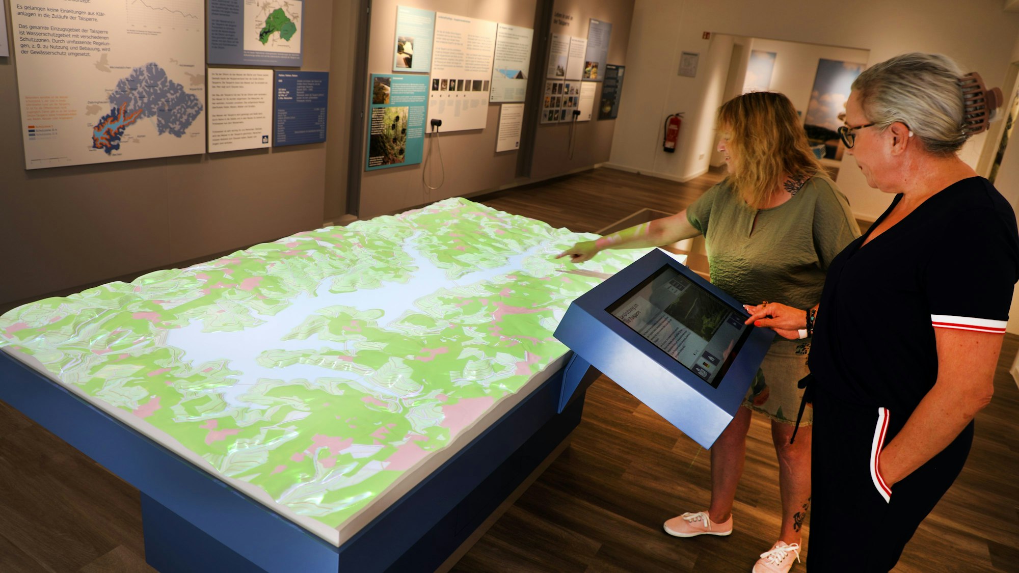 Zwei Frauen stehen an einem Projektionspult in der Ausstellung „Wasser verbindet“ im neuen Aqualon-Forum am Staudamm der Großen Dhünn-Talsperre.