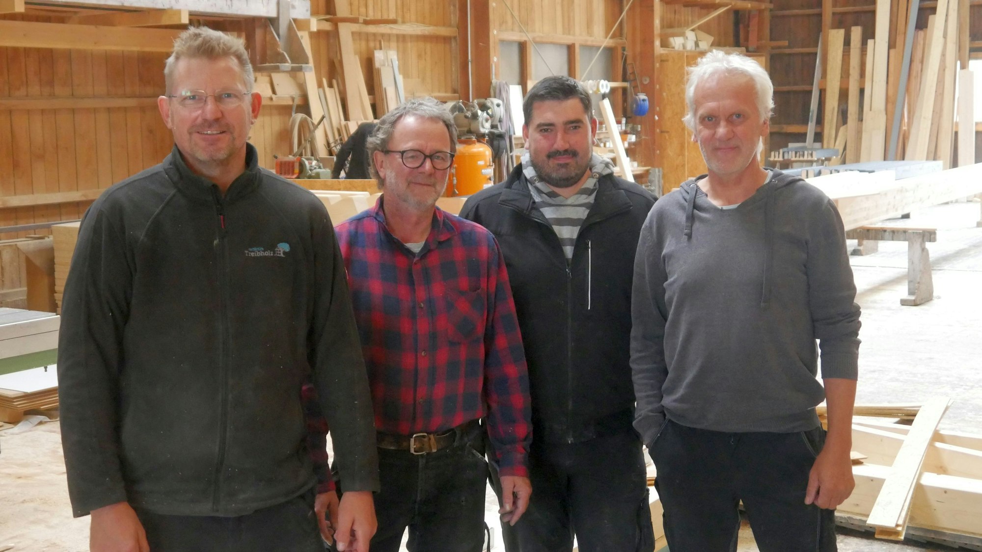 Vier Männer stehen in einer Halle mit Holz.