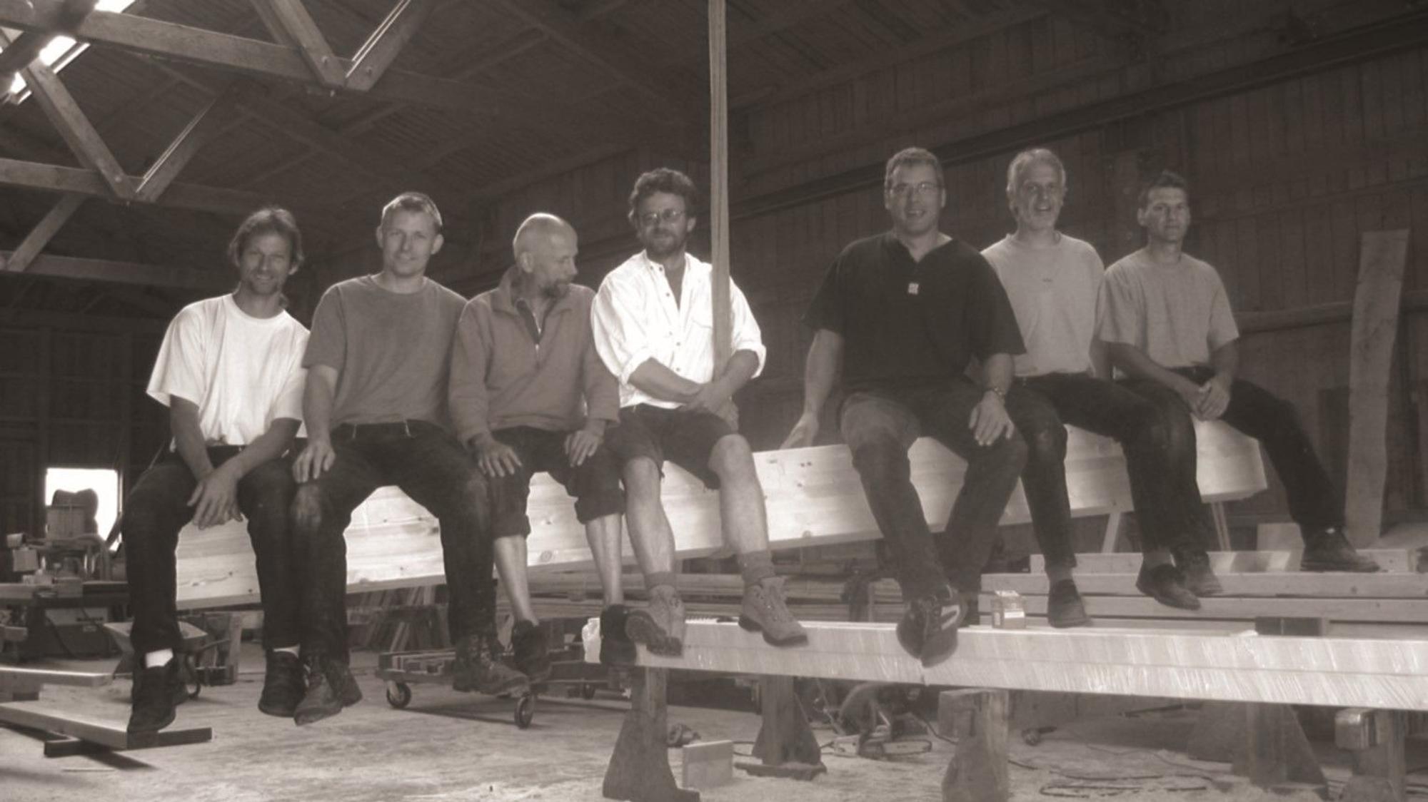 Ein Schwarz-Weiß-Foto von Männern, die auf einem großen Holzbalken sitzen.