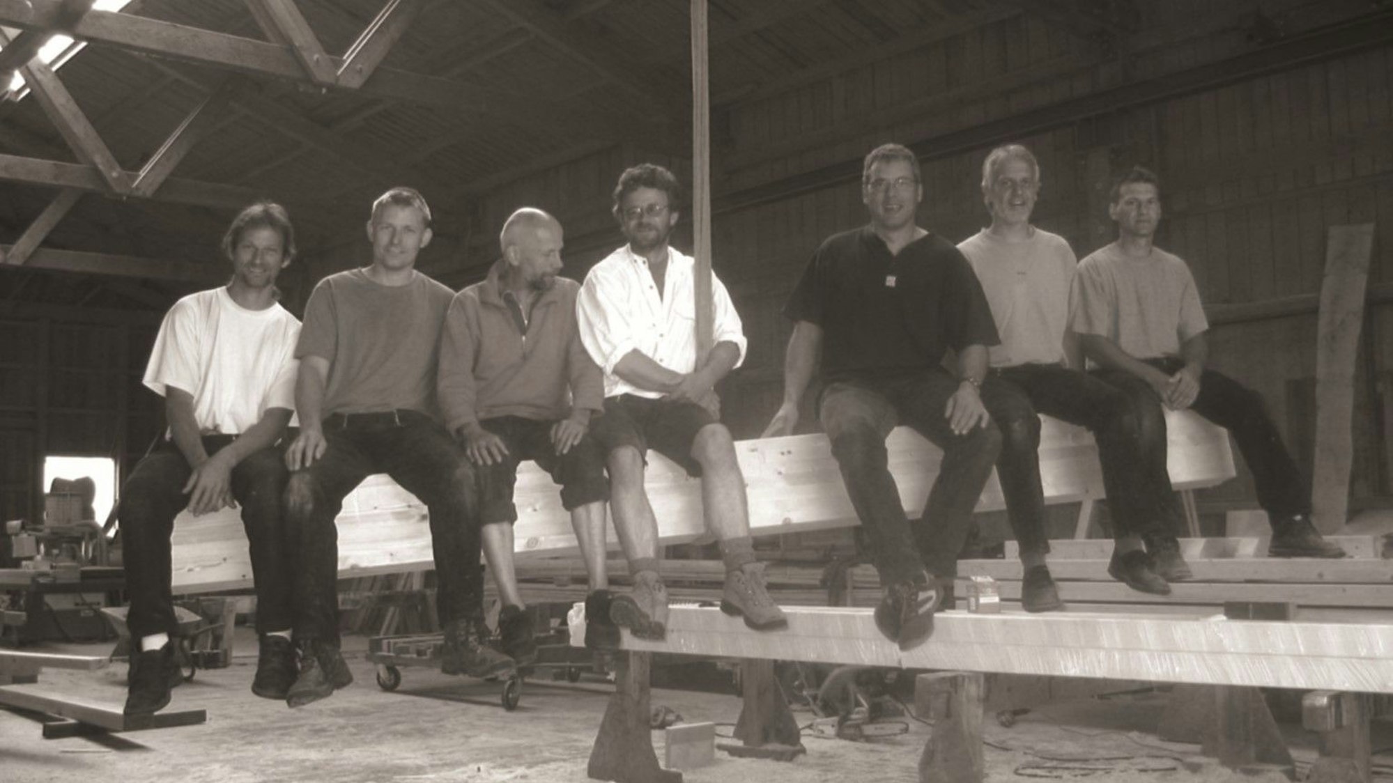 Ein Schwarz-Weiß-Foto von Männern, die auf einem großen Holzbalken sitzen.