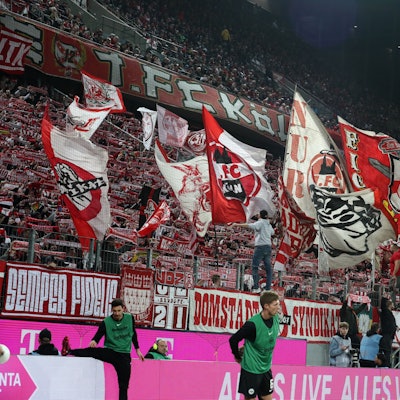 Auf einer Tribüne halten Fußball-Fans rot-weiße Schals hoch und schwenken Fahnen.
