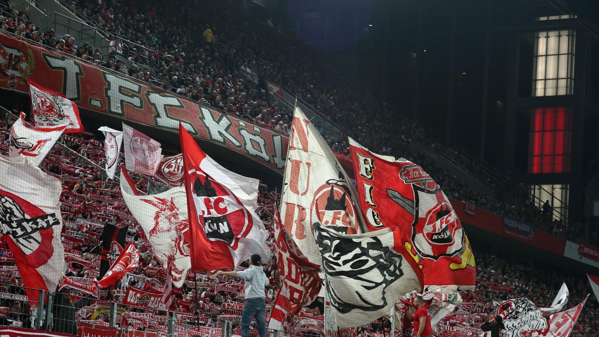 Auf einer Tribüne halten Fußball-Fans rot-weiße Schals hoch und schwenken Fahnen.