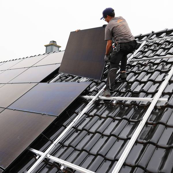 Zu sehen ist ein Handwerker, der auf dem Dach eines Wohnhauses Solarmodule montiert.