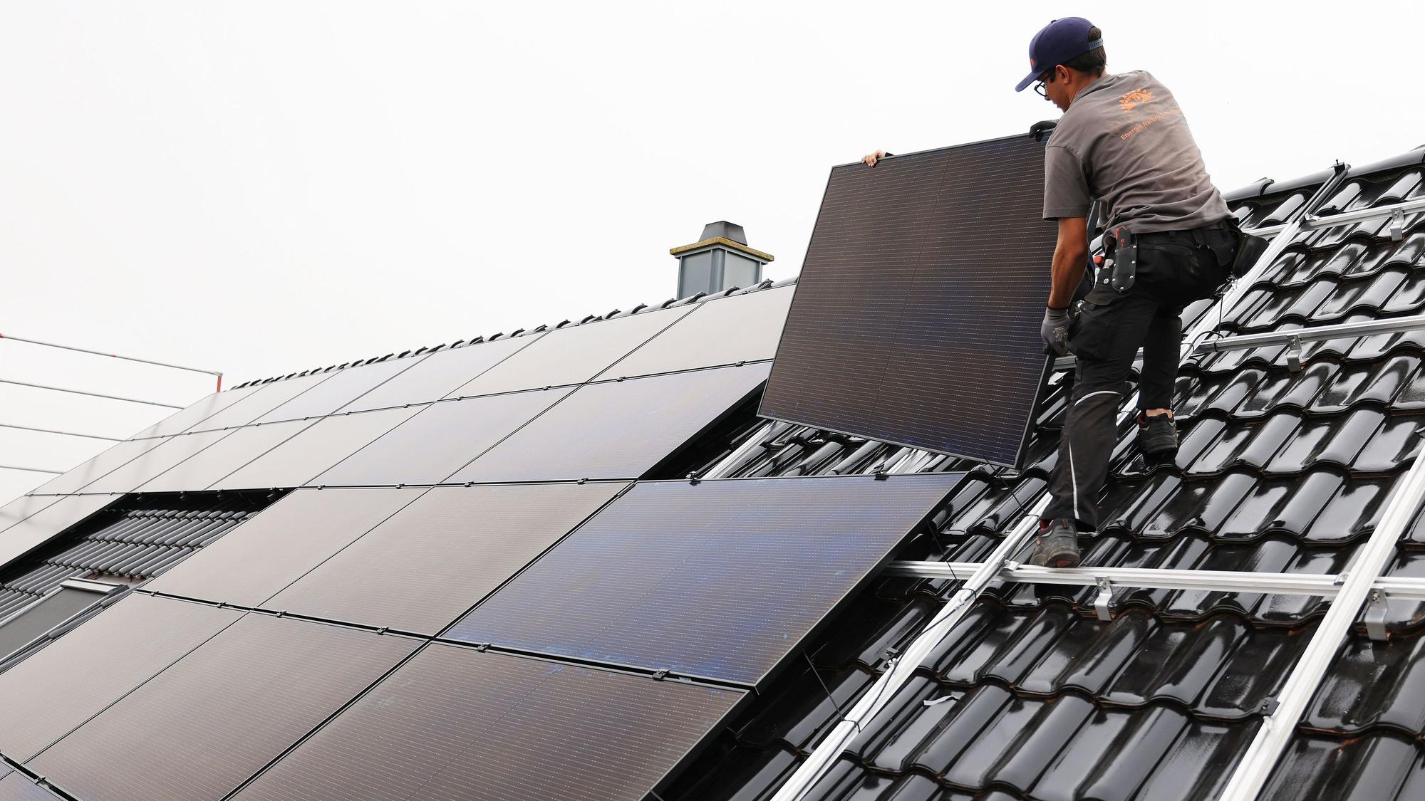 Zu sehen ist ein Handwerker, der auf dem Dach eines Wohnhauses Solarmodule montiert.