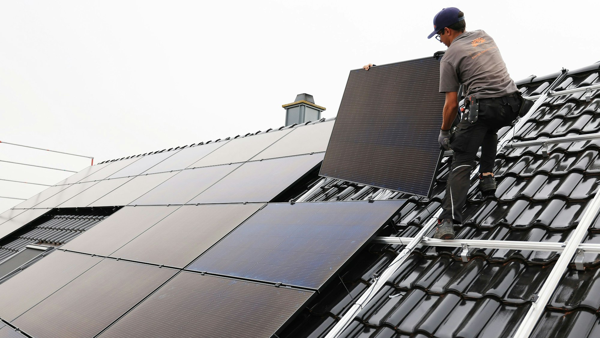 Zu sehen ist ein Handwerker, der auf dem Dach eines Wohnhauses Solarmodule montiert.