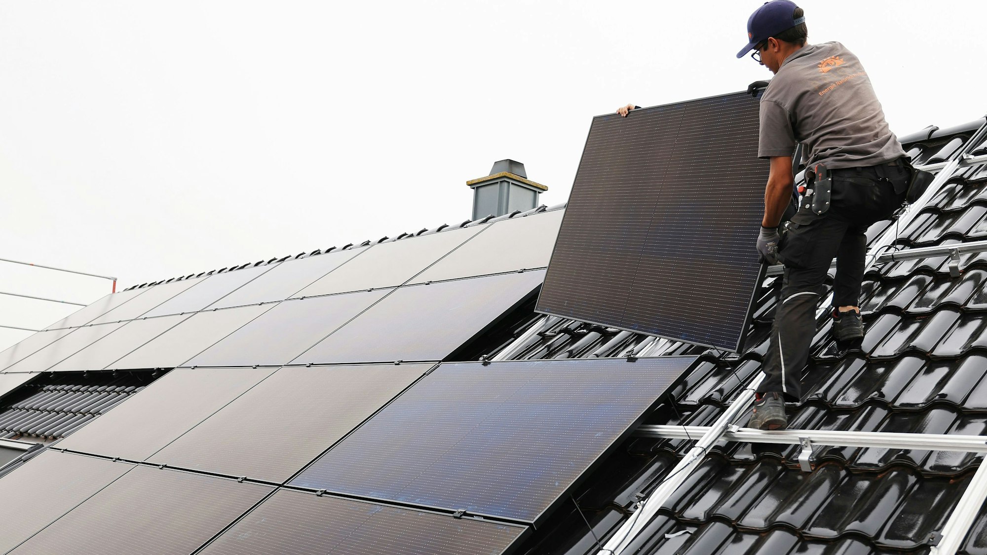 Handwerker montieren Solarmodule auf dem Dach eines Wohnhauses.
