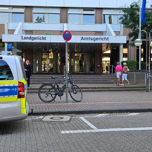 Das Foto zeigt den Eingang zum Gerichtskomplex in Köln. Ein Polizeiwagen steht davor.