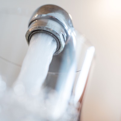Wasser läuft aus einem Wasserhahn in ein Glas.