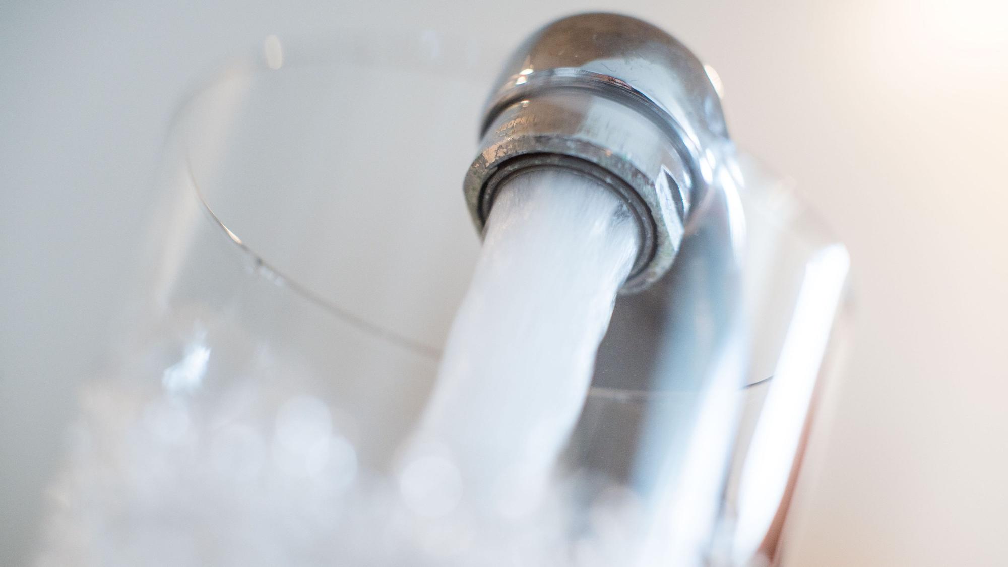 Wasser läuft aus einem Wasserhahn in ein Glas.