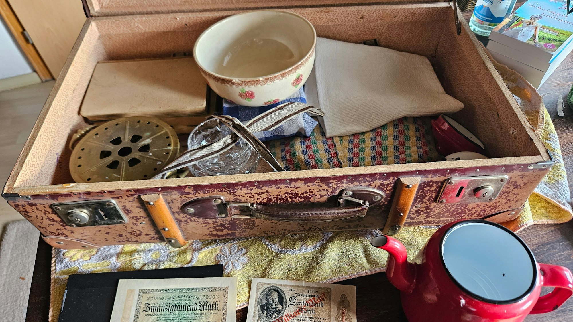 Ein Koffer mit Tüchern, einer Kaffeekanne und alten Geldscheinen ist zu sehen.