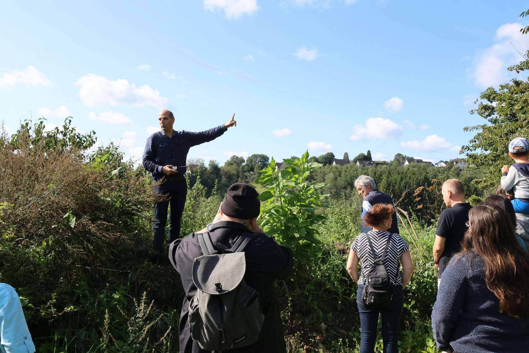 Die Gruppe der Interessierten ist auf einer Anhöhe oberhalb des Hallenbades „Monte Mare“ in Reichshof-Eckenhagen angekommen. Dort nimmt Investor Markus Lüdorf – mit dem Finger zeigend – Stellung zum geplanten Parkplatz für die Sommerrodelbahn.