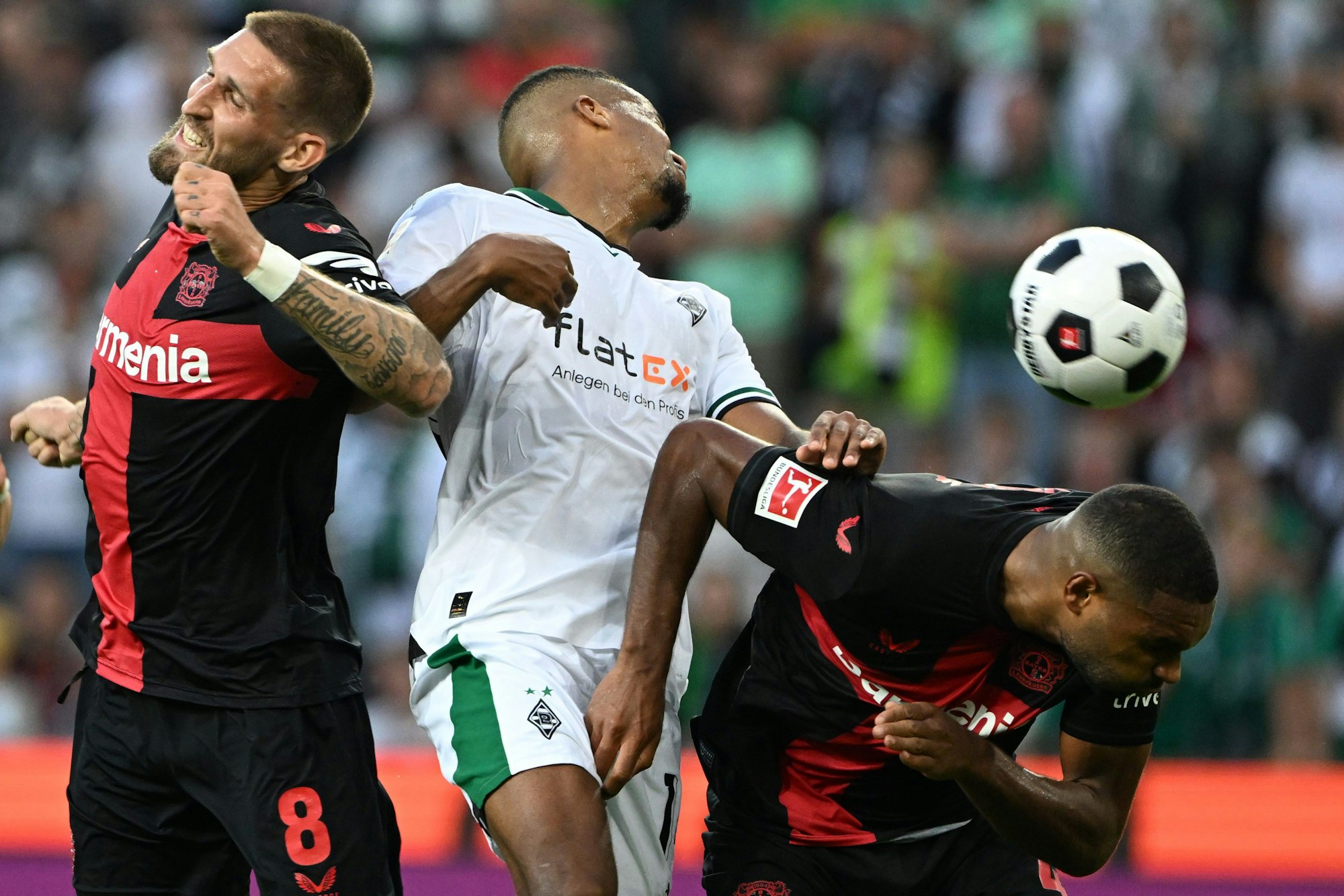 Mönchengladbachs Alassane Plea (M) und Leverkusens Robert Andrich (l) und Jonathan Tah (r) kämpfen um den Ball.