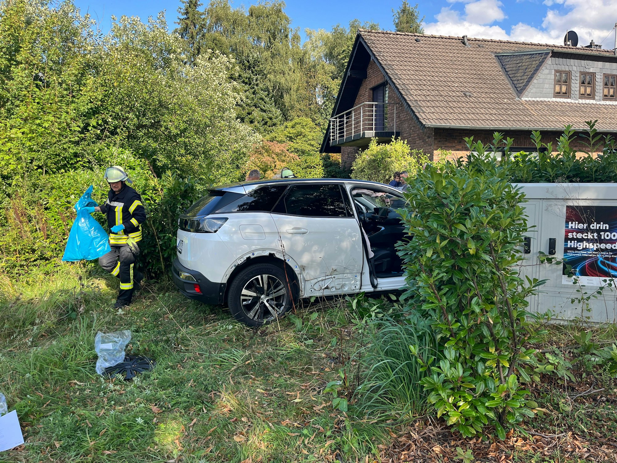 Bei einem Verkehrsunfall in Ruppichteroth sind vier Menschen verletzt worden, einer davon schwer. Ein Auto durchbrach eine Kirschlorbeer-Hecke. Ein Feuerwehrmann sammelte medizinischen Abfall ein.
